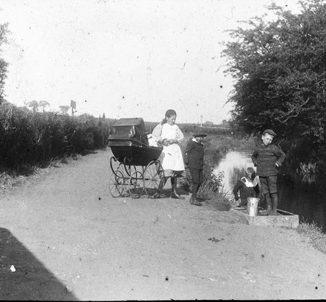 Crayford - opposite Princesses. Children are by the river with an adult woman, who pushes a pram. | Bexley Local Studies & Archive Centre